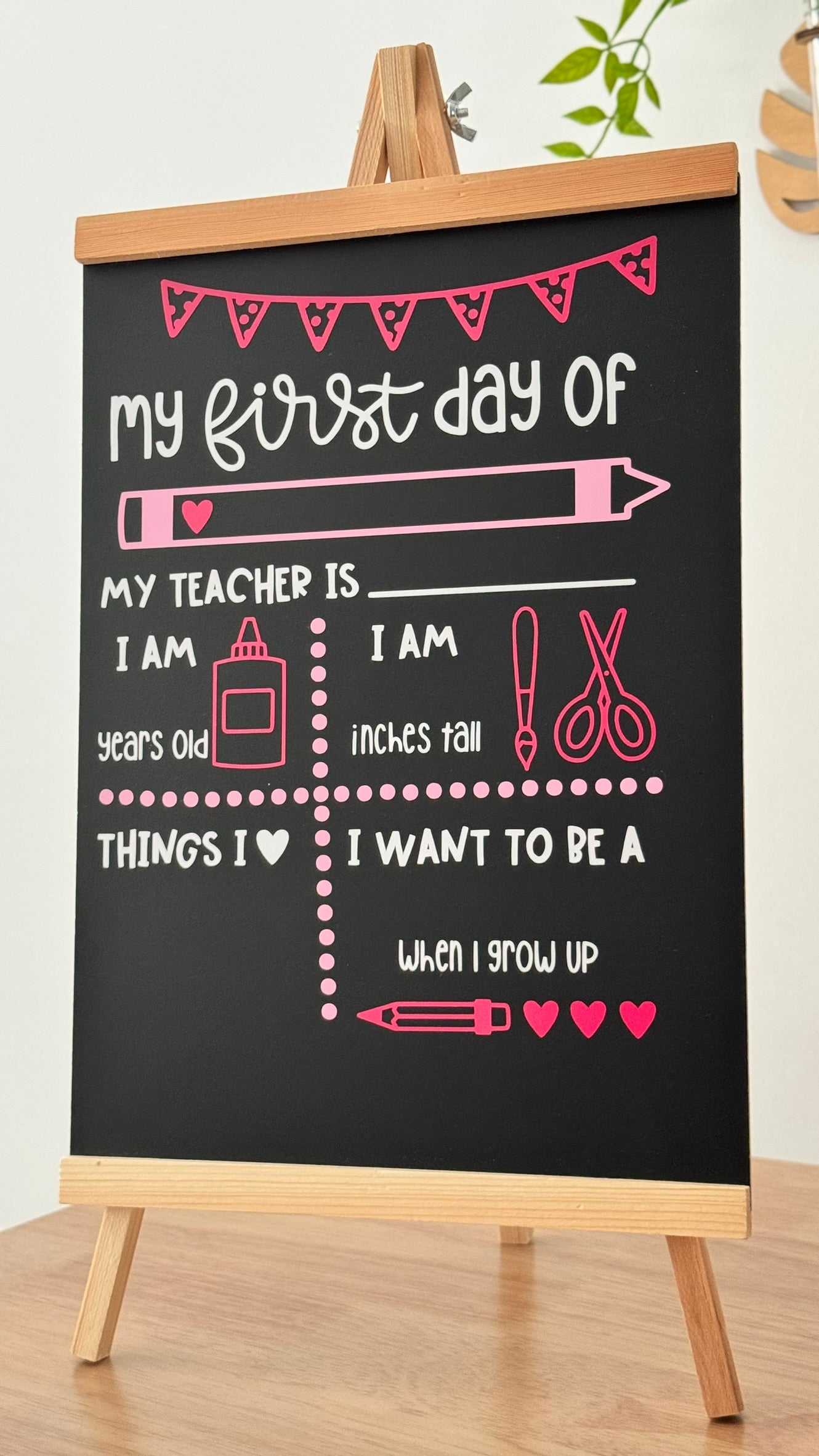 Blackboard with pink text and graphics on a wooden stand, used for 'My First Day of School' theme.
