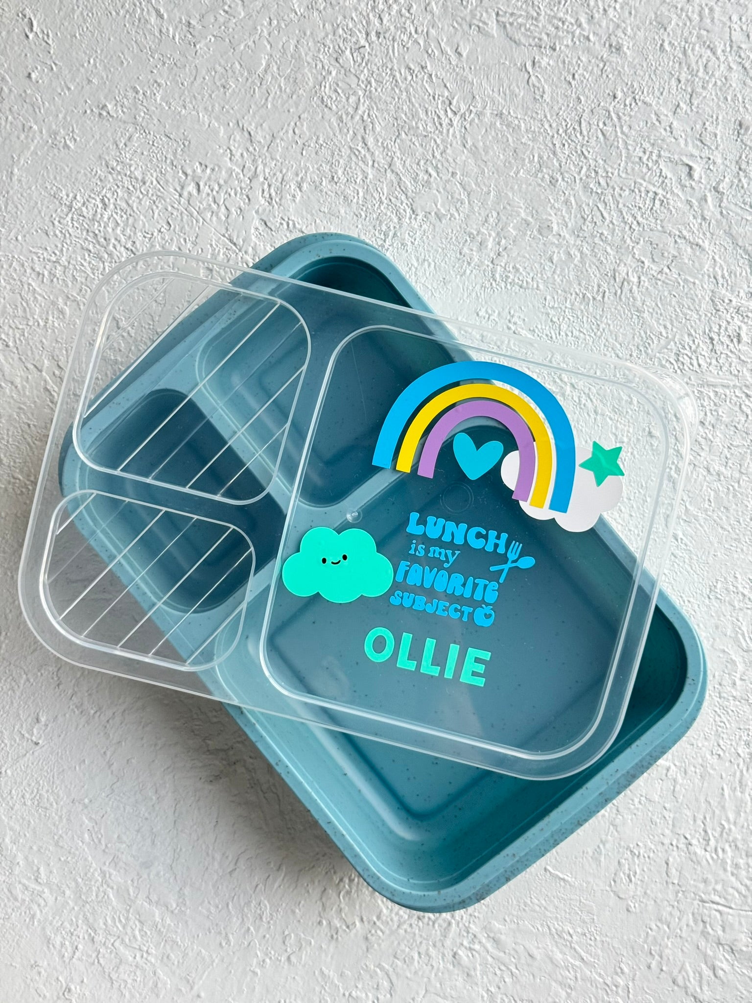 Blue bento box with a personalized sticker on a white background.
Personalized kids lunch box customized with child's name | Custom lunch box in the UAE.

